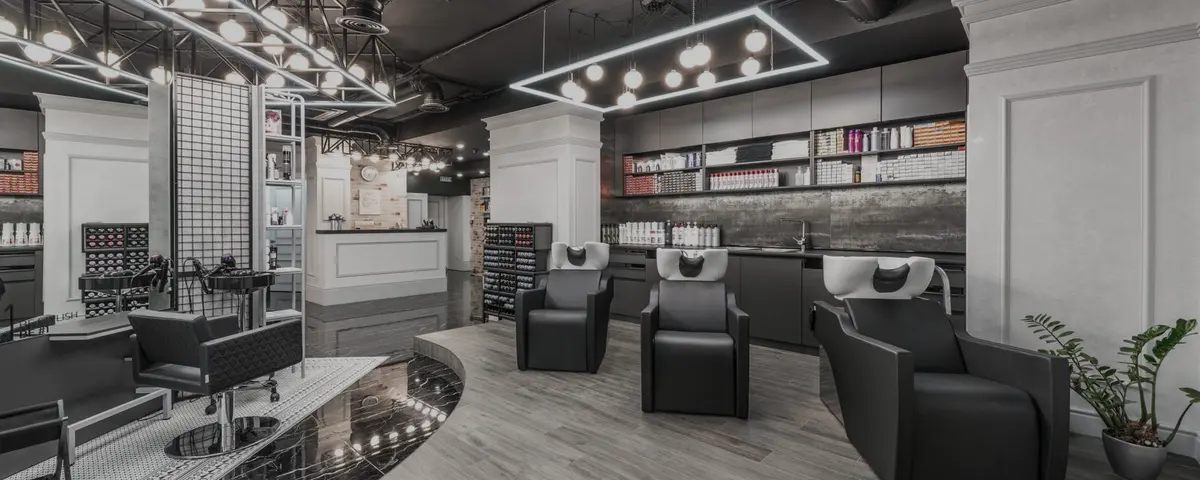 Een kapsalon met de stoelen op een rij, de wasbakken achteraan en de producten op de rekken langs de wand.