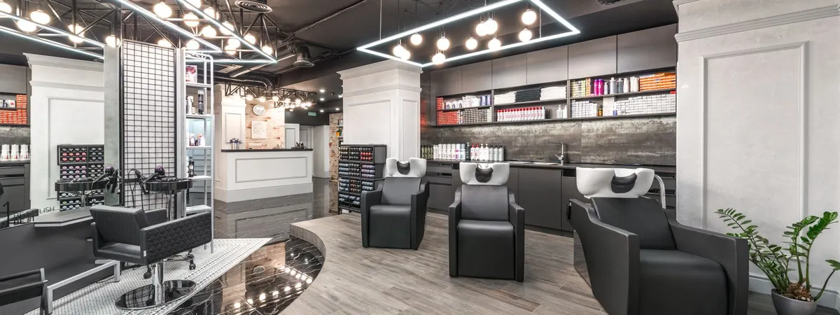 Een kapsalon met de stoelen op een rij, de wasbakken achteraan en de producten op de rekken langs de wand.